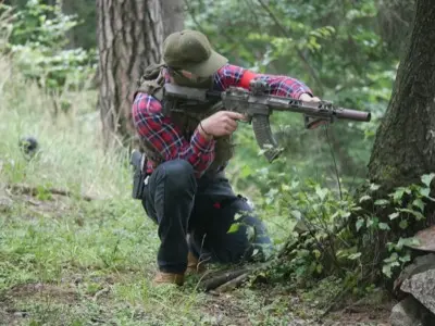 Airsoftový hráč při krytí za stromem během lesního tréninku
